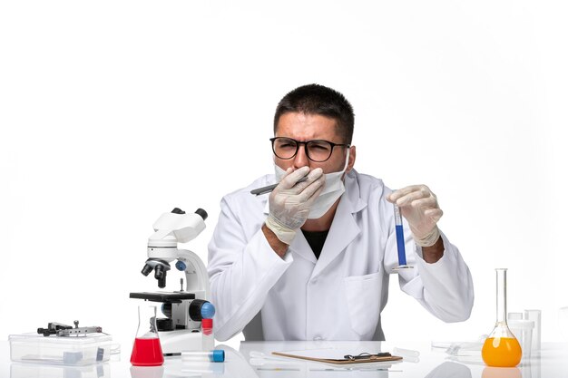 Vue avant de l'homme médecin en costume médical blanc et avec masque travaillant avec une solution sur un espace blanc