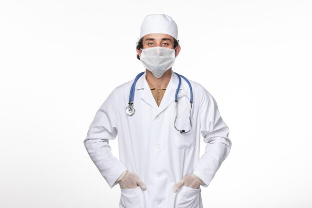 Vue avant de l'homme médecin en costume médical avec masque comme protection contre le covid sur la médecine pandémique du virus coronavirus mur blanc