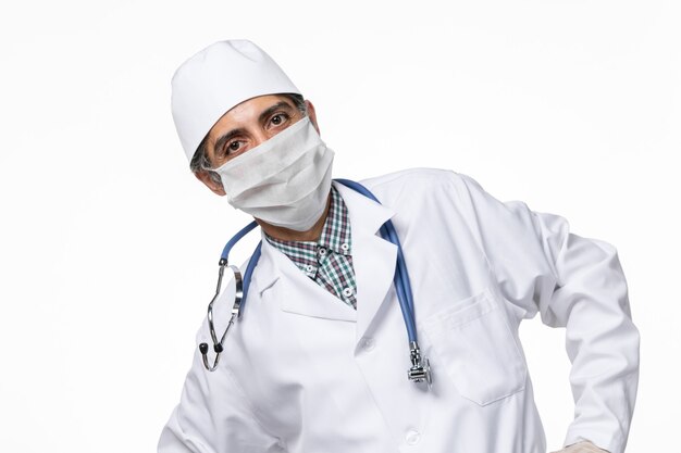 Vue avant de l'homme médecin en costume médical avec masque en raison de covid- sur un bureau blanc