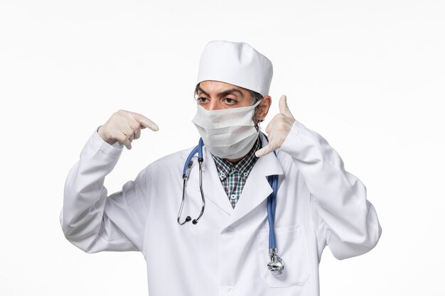 Vue avant de l'homme médecin en costume médical avec masque en raison de covid- sur un bureau blanc