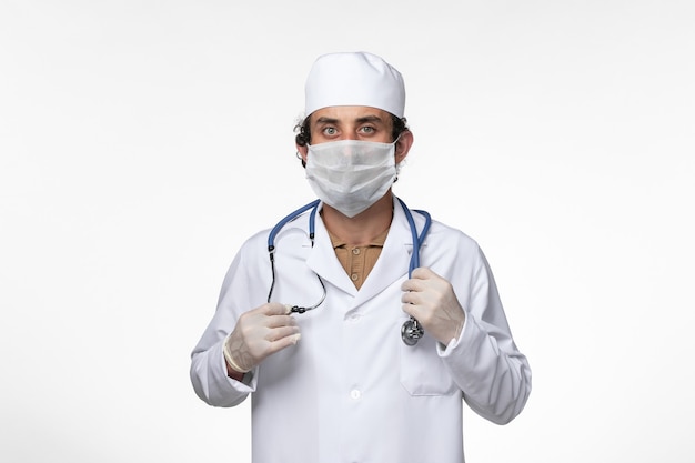 Vue avant de l'homme médecin en costume médical et portant un masque comme une protection contre les covid- sur le bureau blanc virus de la maladie covid- pandémie