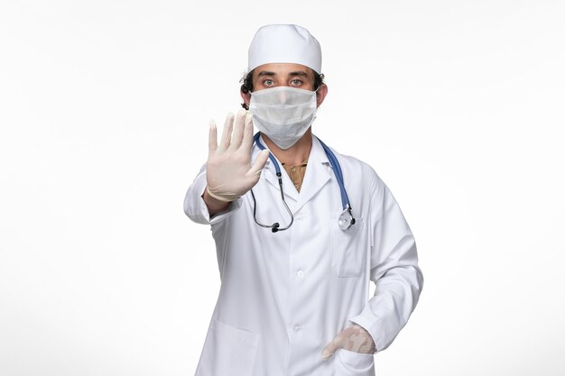 Vue avant de l'homme médecin en costume médical portant un masque comme protection contre les covid- sur la maladie du virus du mur blanc covid- pandémie