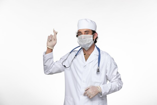 Vue avant de l'homme médecin en costume médical portant un masque comme une protection contre le virus covid- sur mur blanc virus de la santé covid- pandémie