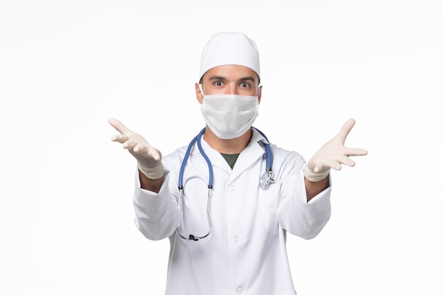 Vue avant de l'homme médecin en costume médical et portant un masque contre covid- sur blanc bureau covid- maladie pandémique de la médecine virale