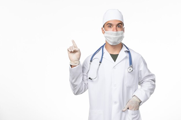 Vue avant de l'homme médecin en costume médical et portant un masque contre covid sur le mur blanc clair maladie à virus covid médecine pandémie
