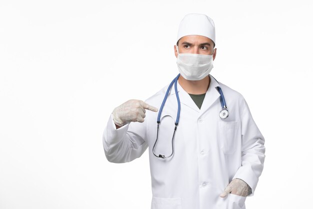 Vue avant de l'homme médecin en costume médical et portant un masque contre covid sur mur blanc pandémie de médecine du virus covid