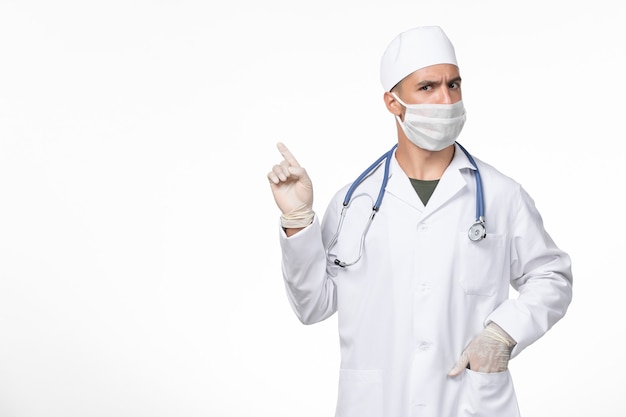 Vue avant de l'homme médecin en costume médical et portant un masque contre covid sur mur blanc pandémie de médecine de maladie à virus covid