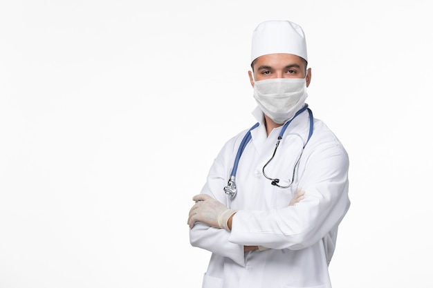 Vue avant de l'homme médecin en costume médical et portant un masque contre covid sur mur blanc virus covid- pandémie de maladie de maladie