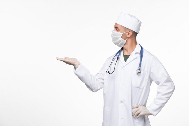 Vue avant de l'homme médecin en costume médical et portant un masque contre covid avec stéthoscope sur mur blanc virus covid- maladie pandémie de maladie