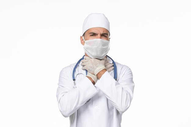 Vue avant de l'homme médecin en costume médical et portant un masque en raison de covid- sur le bureau blanc covid- maladie à virus pandémique
