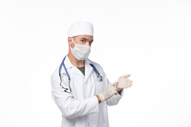 Vue avant de l'homme médecin en costume médical et portant un masque en raison de covid- sur la maladie du mur blanc covid- maladie à virus pandémique