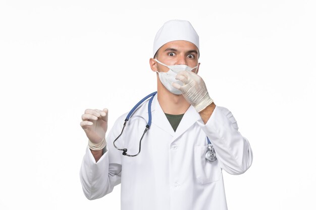 Vue avant de l'homme médecin en costume médical et portant un masque en raison de covid- sur la maladie du mur blanc covid- pandémie