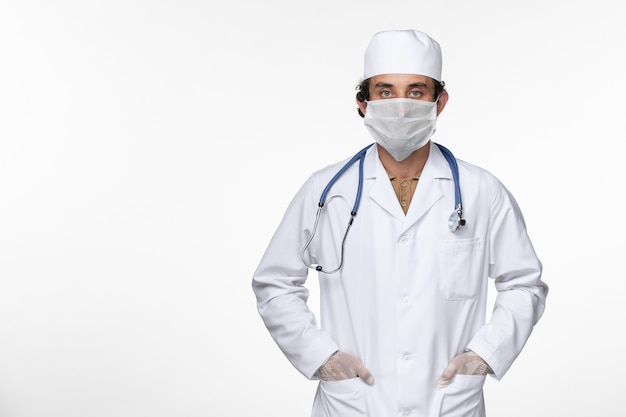Vue avant de l'homme médecin en costume médical portant un masque stérile comme une protection contre la maladie pandémique du coronavirus virus covid- sur bureau blanc