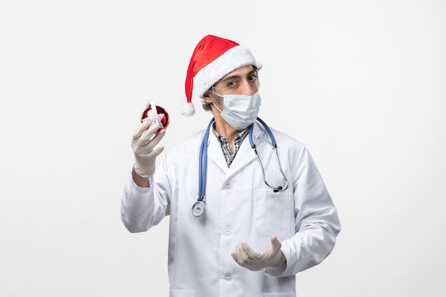 Vue avant de l'homme médecin en masque avec jouet sur mur blanc virus covid vacances santé