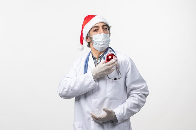 Vue avant de l'homme médecin en masque avec jouet sur mur blanc virus covid vacances santé