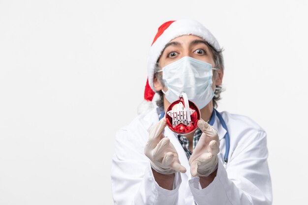 Vue avant de l'homme médecin en masque avec jouet sur sol blanc virus de la nouvelle année covid santé