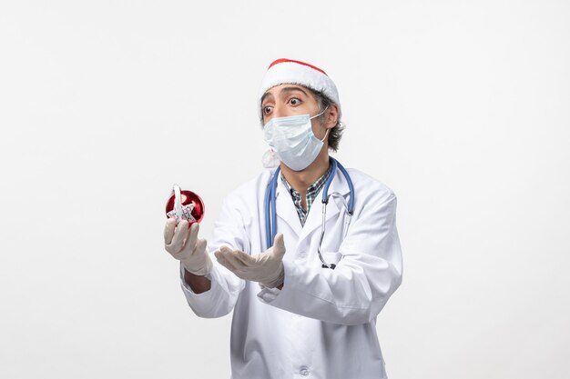 Vue avant de l'homme médecin en masque avec jouet sur sol blanc virus de vacances covid santé