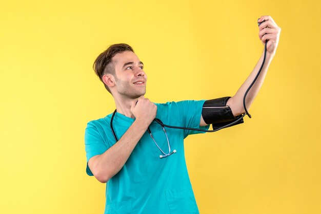 Vue avant de l'homme médecin mesurant la pression sur le mur jaune