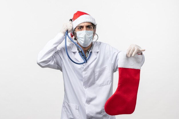 Vue avant de l'homme médecin observant la chaussette de vacances sur le mur blanc de la santé de vacances virus covid