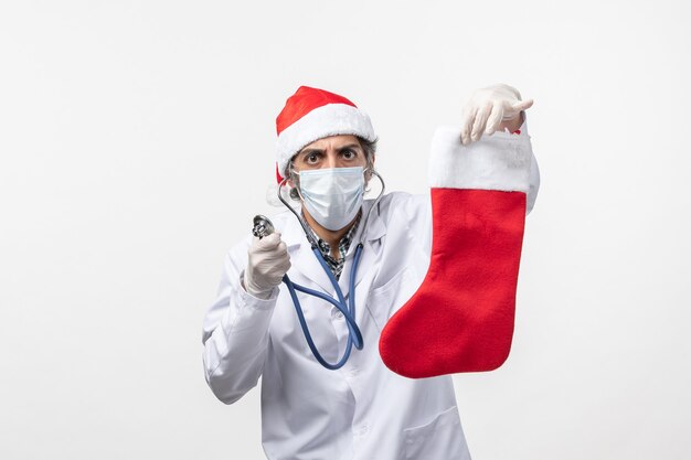 Vue avant de l'homme médecin observant la chaussette de vacances sur le mur blanc de la santé de vacances virus covid