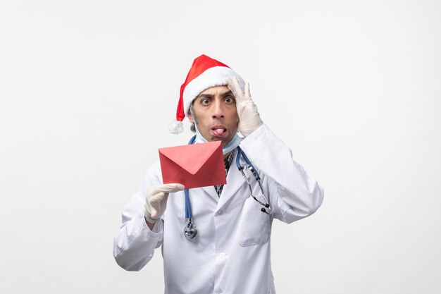 Vue avant de l'homme médecin tenant une enveloppe rouge sur le virus de la santé de mur blanc covid-