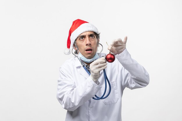 Vue avant de l'homme médecin tenant jouet sur mur blanc virus covid santé nouvelle année