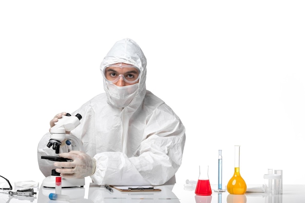 Vue avant de l'homme médecin en tenue de protection avec masque en raison de covid à l'aide d'un microscope sur un espace blanc