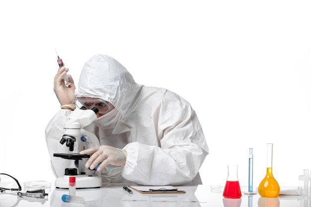 Vue avant de l'homme médecin en tenue de protection avec masque en raison de covid à l'aide d'un microscope sur un espace blanc