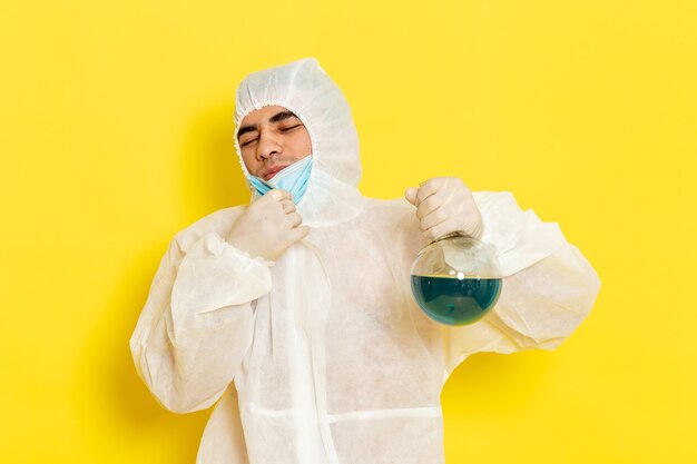 Vue Avant De L'homme Travailleur Scientifique En Combinaison De Protection Spéciale Holding Flask Avec Solution Bleue Décoller Son Masque Sur La Surface Jaune