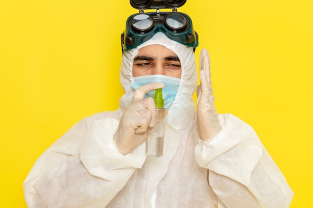 Photo gratuite vue avant de l'homme travailleur scientifique en combinaison de protection spéciale holding spray en l'utilisant sur une surface jaune