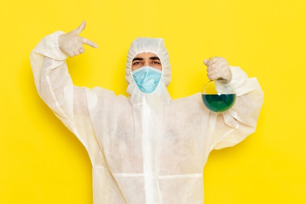 Photo gratuite vue avant de l'homme travailleur scientifique en combinaison de protection spéciale tenant le ballon avec une solution bleue sur une surface jaune clair