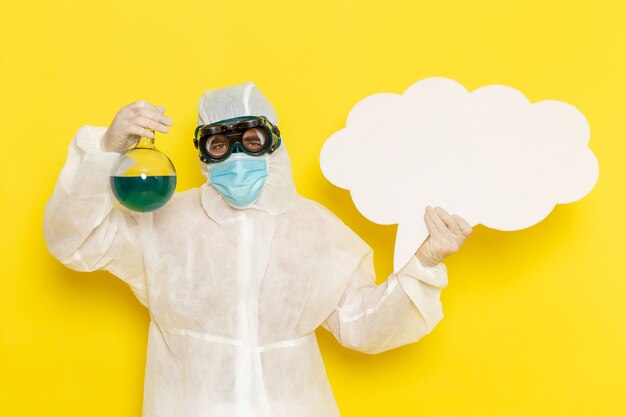 Vue avant de l'homme travailleur scientifique en costume spécial holding flask avec solution verte et grand panneau blanc sur bureau jaune