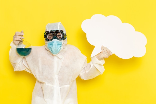 Vue avant de l'homme travailleur scientifique en costume spécial holding flask avec solution verte et grand panneau blanc sur bureau jaune