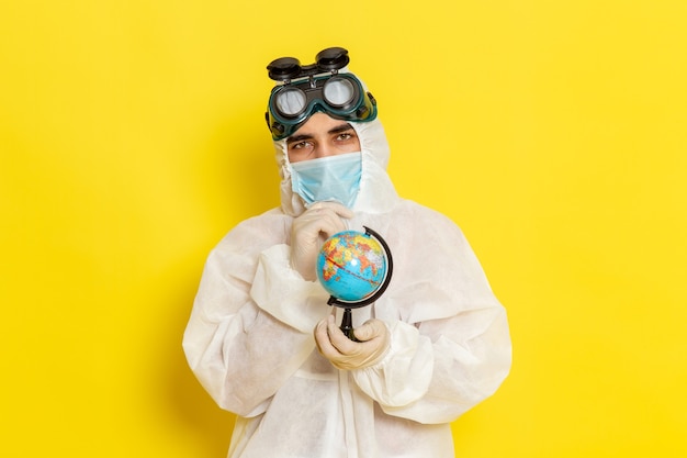 Photo gratuite vue avant de l'homme travailleur scientifique en costume spécial tenant petit globe sur un bureau jaune