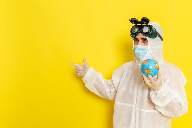 Vue avant de l'homme travailleur scientifique en costume spécial tenant petit globe rond sur un bureau jaune