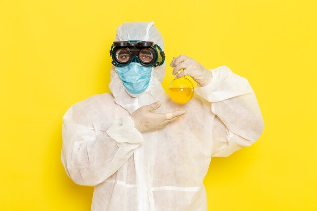 Vue avant de l'homme travailleur scientifique en tenue de protection spéciale tenant le ballon avec une solution jaune sur une surface jaune