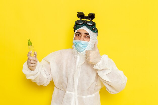 Vue avant de l'homme travailleur scientifique en tenue de protection spéciale tenant flacon pulvérisateur sur la surface jaune clair