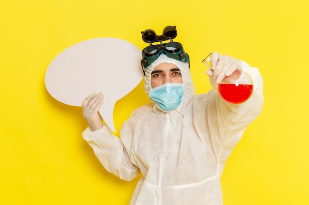 Vue avant de l'homme travailleur scientifique en tenue de protection spéciale tenant flacon avec solution rouge et panneau blanc sur surface jaune