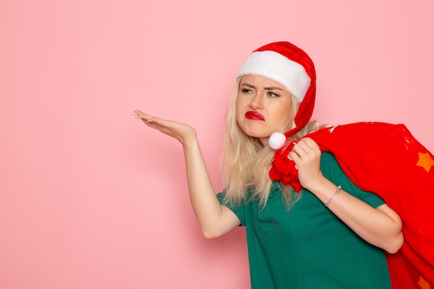 Vue avant jeune femme transportant un sac rouge avec des cadeaux sur le mur rose modèle Noël nouvel an couleur vacances santa