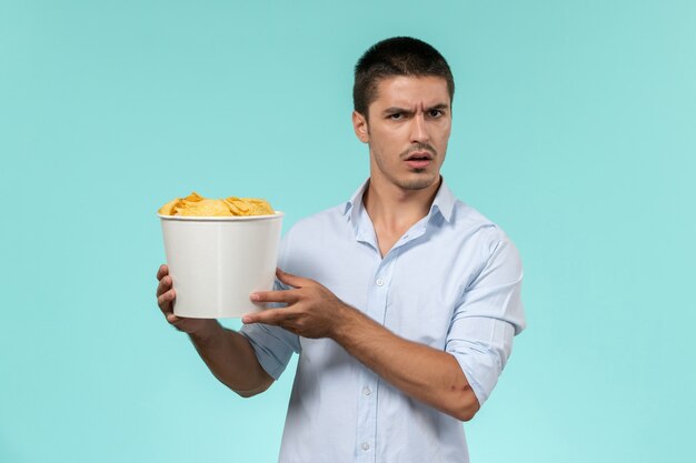 Vue avant, jeune homme, tenue, panier, à, cips, sur, mur bleu clair, film, télécommande, cinéma, cinéma, théâtre
