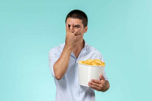 Vue avant, jeune homme, tenue, panier, à, pomme terre cips, sur, les, mur bleu, lonely, remote male movie cinema