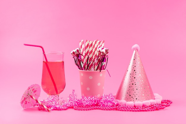 Photo gratuite une vue avant de jus de fruits frais avec de la paille avec chapeau d'anniversaire et bonbons stick sur rose