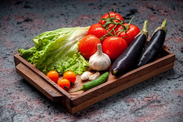 Vue avant de légumes frais tomates rouges ail salade verte et aubergines à l'intérieur de la planche de bois sur fond bleu
