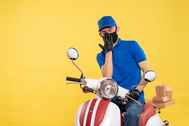 Vue avant messager masculin assis sur le vélo en masque sur le travail de livraison pandémie jaune covid- travail de service