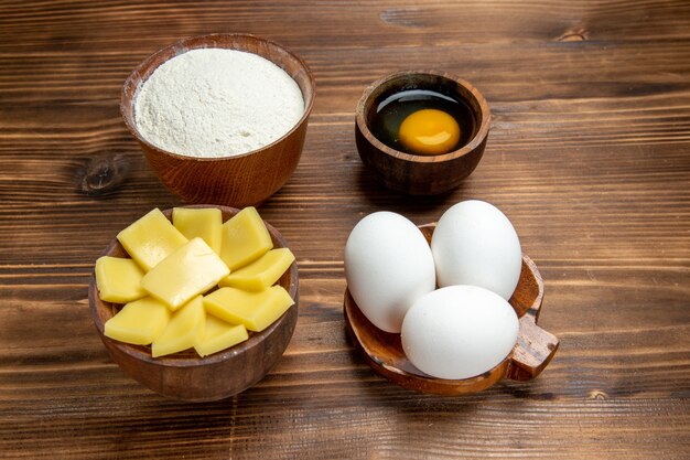 Vue avant des oeufs crus entiers avec de la farine de fromage sur la table en bois brun produit pâte à l'oeuf pâte