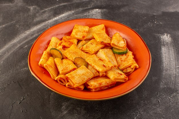 Une vue avant de pâtes italiennes cuites avec sauce tomate et concombre à l'intérieur de la plaque sur la surface sombre