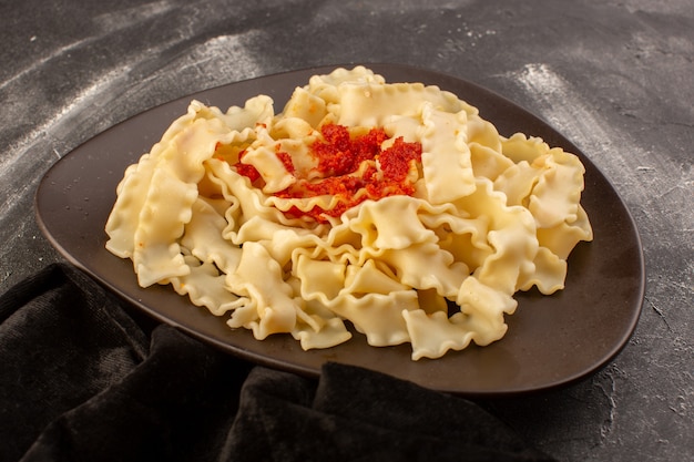 Une vue avant des pâtes italiennes cuites avec sauce tomate à l'intérieur de la plaque sur la surface grise