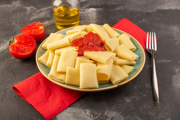 Une vue avant des pâtes italiennes cuites avec sauce tomate à l'intérieur de la plaque sur la table grise des pâtes alimentaires repas italien