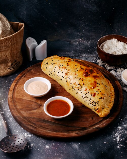 Vue avant de la pâtisserie cuite avec des sauces rouges et blanches sur le bureau rond en bois brun et le plancher gris