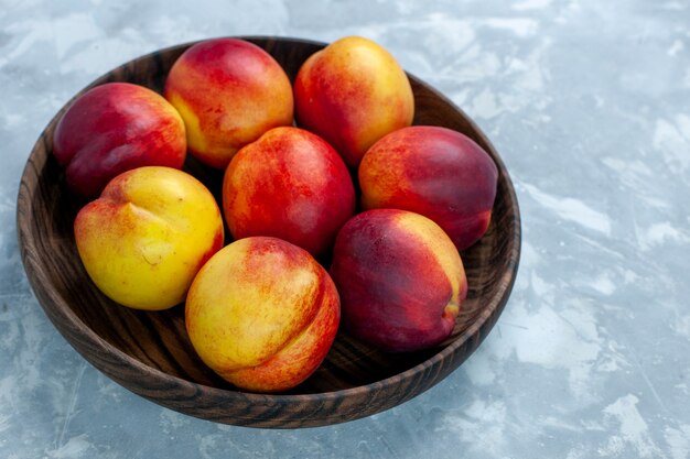 Vue avant des pêches fraîches fruits moelleux et savoureux à l'intérieur de la plaque brune sur un bureau blanc clair